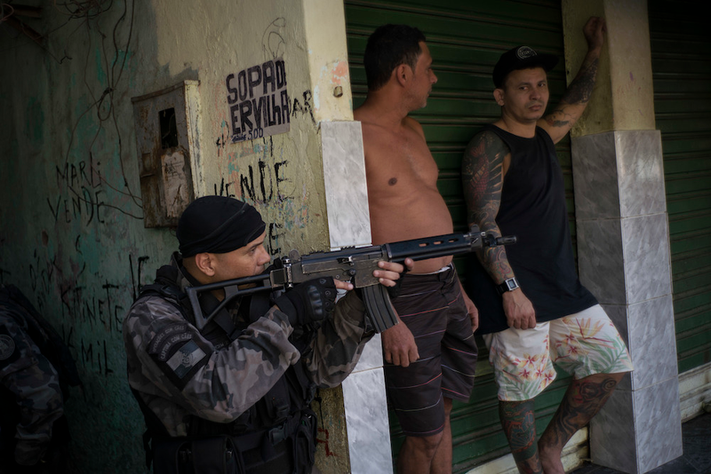 “A police officer takes position near residents during an operation against drug traffickers at the ‘pacified’ Jacarezinho slum in Rio de Janeiro, Brazil.”